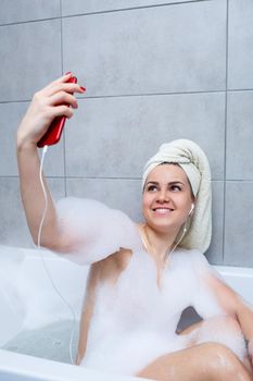 Beautiful young woman listening to music and singing while taking a bath at home. Relax after a hard day. Spa relaxing procedure.
