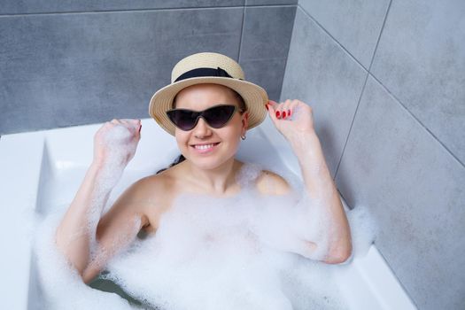 Young woman in a hat and sunglasses takes a bath at home. Relax after a hard day. The spa is a relaxing procedure.