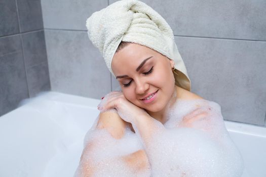 Girl woman with a white towel on her head lies in the bathroom in a white bath. Foam for around. Relax after a hard day. Spa relaxing treatment