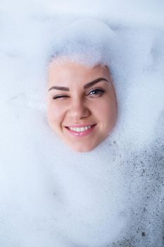 Closeup portrait of a girl in a bathtub and white foam around her face. Different emotions, grimaces, woman smile