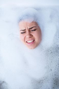 Closeup portrait of a girl in a bathtub and white foam around her face. Different emotions, grimaces, woman smile