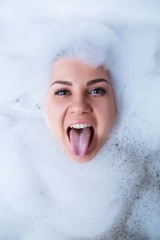 Closeup portrait of a girl in a bathtub and white foam around her face. Different emotions, grimaces, woman smile