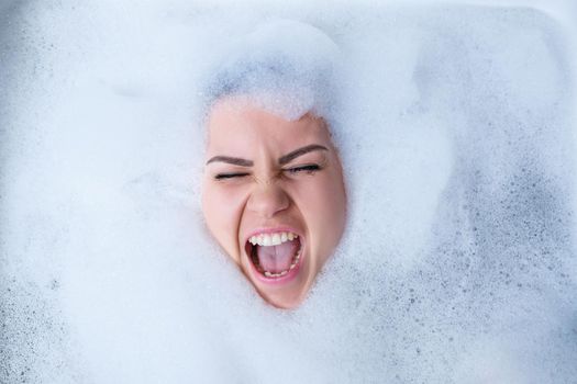 Closeup portrait of a girl in a bathtub and white foam around her face. Different emotions, grimaces, woman smile