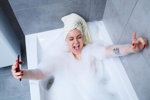 Beautiful young woman listening to music and singing while taking a bath at home. Relax after a hard day. Spa relaxing procedure.