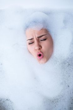 Closeup portrait of a girl in a bathtub and white foam around her face. Different emotions, grimaces, woman smile