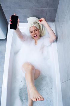 Beautiful young woman listening to music and singing while taking a bath at home. Relax after a hard day. Spa relaxing procedure.