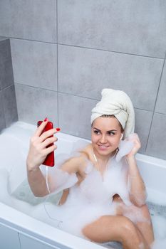 Beautiful young woman listening to music and singing while taking a bath at home. Relax after a hard day. Spa relaxing procedure.