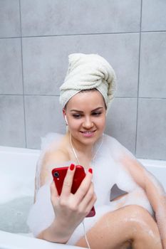Beautiful young woman listens to music with headphones and sings while taking a bath at home. Relax after a hard day. Relaxing spa treatment.