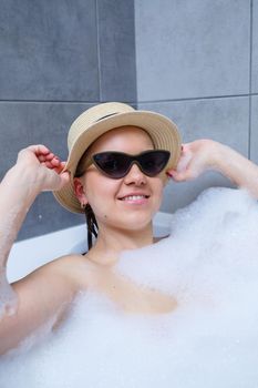 Young woman in a hat and sunglasses takes a bath at home. Relax after a hard day. The spa is a relaxing procedure.
