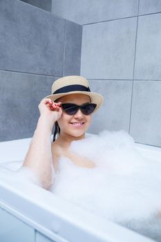 Young woman in a hat and sunglasses takes a bath at home. Relax after a hard day. The spa is a relaxing procedure.
