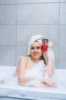 Beautiful young woman with a towel on her head drinking a cocktail takes a bath at home. Relax after a hard day. The spa is a relaxing procedure.