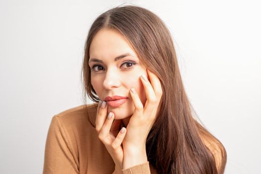 Portrait of the caucasian female model touching face with manicured fingers isolated on white background