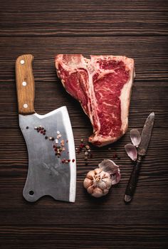 Top view of raw fresh marbled meat steak T-bone, rustic meat cleaver, seasonings on wooden background. Cooking juicy organic steak/butchery concept, healthy clean eating, close up