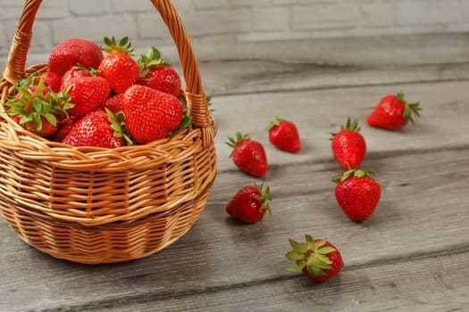 Basket with strawberries, some of them spilled on gray wood desk.