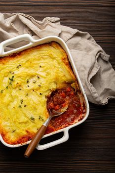 Traditional dish of British cuisine Shepherd's pie casserole with minced meat and mashed potatoes in ceramic baking dish on white rustic table with spoon from above