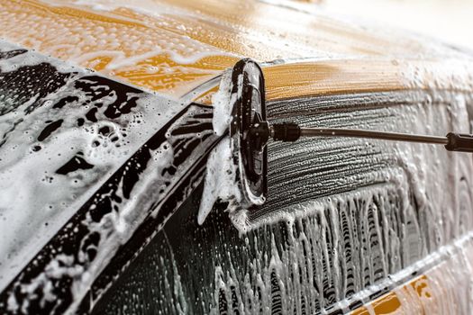 Side of yellow car being washed in self serve carwash, Brush leaving strokes on glass in shampoo and foam.