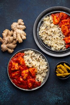 Chicken tikka masala dish with rice, flat Indian bread and spices in rustic metal plates on concrete background top view. Chicken tomato curry, turmeric root, fresh cilantro, traditional Indian meal