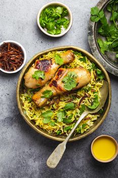 Biryani chicken, traditional dish of Indian cuisine, with basmati rice, fried onion, fresh cilantro in bowl on gray rustic stone background. Authentic Indian meal, top view, close-up