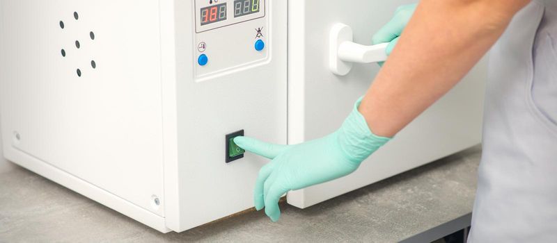 Beautician in protective gloves starts the machine for disinfection of tools before the depilation procedure