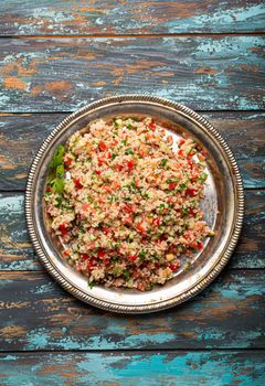 Middle eastern and Mediterranean traditional vegetable salad tabbouleh with couscous on rustic metal plate and wooden background from above. Arab Turkish food.