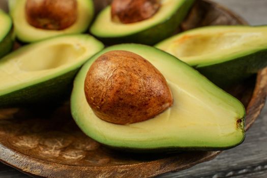 Close up photo of avocado halves on wooden carved bowl, detail on the brown seed / pit.