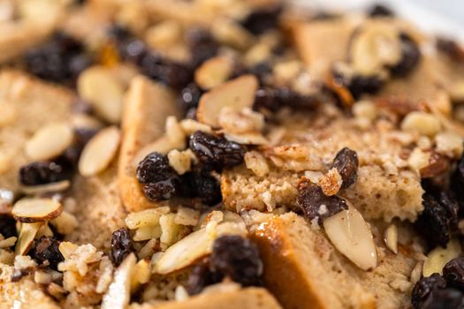 Baking bread pudding with raising and almond slivers in a white casserole dish.