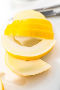 Slicong golden dewlicious melon on a white cutting board.