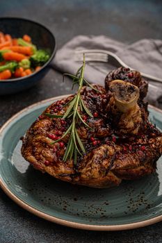 Delicious roasted ham or pork knuckle with glazed brown crispy skin, red pepper berries and rosemary on plate, steamed vegetables on rustic stone table angle view, traditional and festive meal .