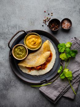 Traditional Indian rice pancakes Dosa with vegetables sambar filling, dips chutney, on metal plate, stone background table. Quick meal or vegetarian snack of South India, top view