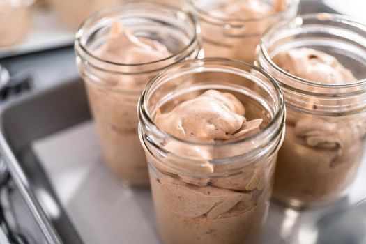 Scooping mixture into the small glass jars to make homemade chocolate ice cream.