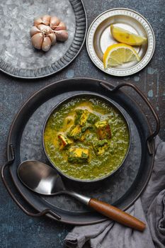 Traditional Indian Punjabi food Palak Paneer with spinach and cheese in vintage metal bowl with spoon on rustic concrete background from above