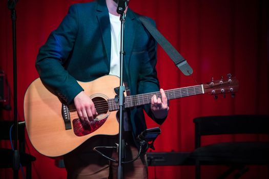 Man plays classical guitar against red curtain