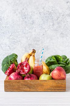 Fruit, greens, vegetables in wooden tray and fresh smoothie or juice in bottle with paper straw on table near white wall, detox, diet, clean eating, vegetarian, healthy food concept .