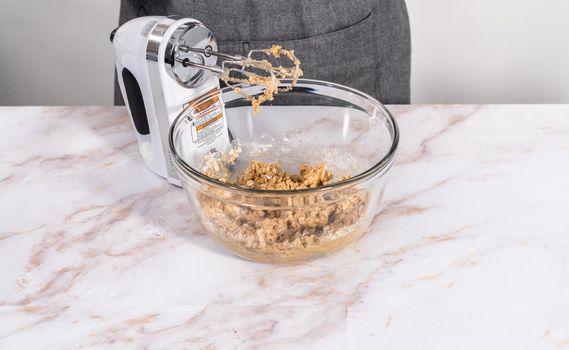 Mixing ingredients in a large glass mixing bowl to bake apple oatmeal cookies.