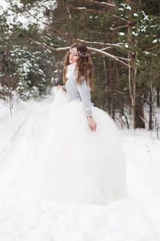 Beautiful bride in a white dress with a bouquet in a snow-covered winter forest. Portrait of the bride in nature.