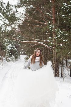 Beautiful bride in a white dress with a bouquet in a snow-covered winter forest. Portrait of the bride in nature.