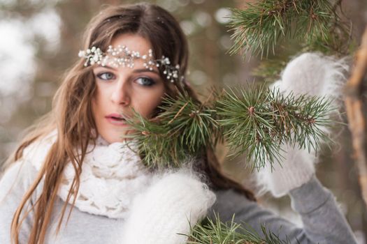 Beautiful bride in a white dress with a bouquet in a snow-covered winter forest. Portrait of the bride in nature.