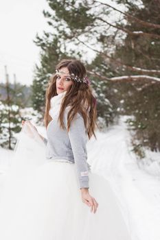 Beautiful bride in a white dress with a bouquet in a snow-covered winter forest. Portrait of the bride in nature.