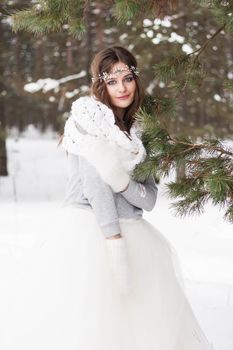 Beautiful bride in a white dress with a bouquet in a snow-covered winter forest. Portrait of the bride in nature.