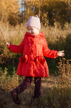 A little girl in a red coat walks in nature in an autumn grove. The season is autumn.