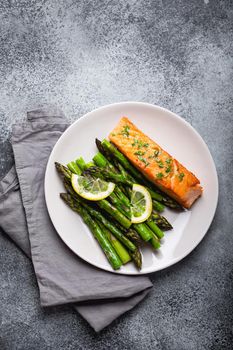 Grilled salmon fillet with green asparagus and seasonings on plate, gray concrete background. Healthy balanced dinner with salmon and asparagus good for diet and wellness, top view, close-up