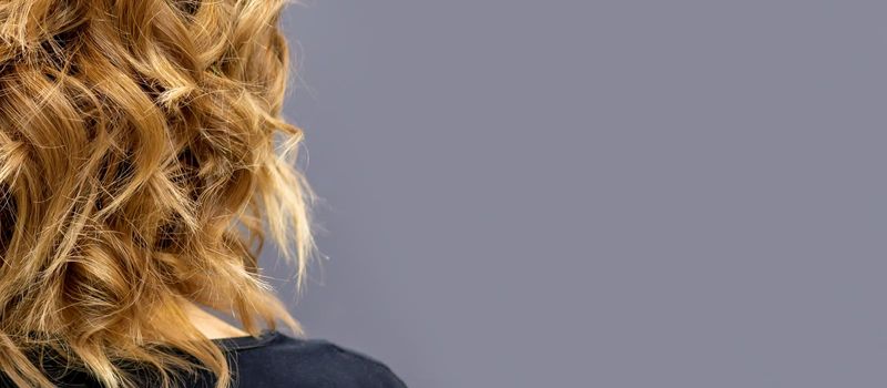 Back view of the woman with long brown curly hair stands on a dark background