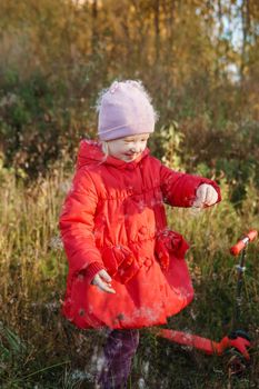 A little girl in a red coat walks in nature in an autumn grove. The season is autumn.