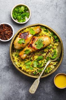 Biryani chicken, traditional dish of Indian cuisine, with basmati rice, fried onion, fresh cilantro in bowl on gray rustic stone background. Authentic Indian meal, top view, close-up