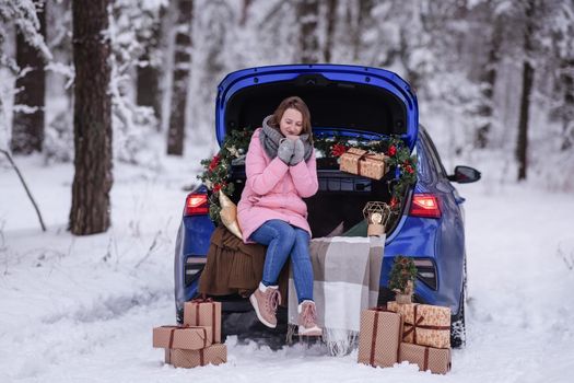 A woman in winter clothes drinks a hot drink sitting in a car decorated in a New Year's way. Traveling by car through the forest. A trip before Christmas.