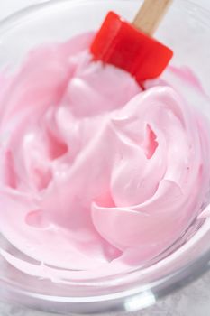 Mixing in food coloring into the meringue to prepare unicorn theme meringue pops.