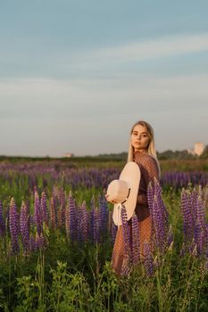 A beautiful woman in a straw hat walks in a field with purple flowers. A walk in nature in the lupin field.