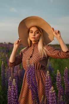 A beautiful woman in a straw hat walks in a field with purple flowers. A walk in nature in the lupin field.