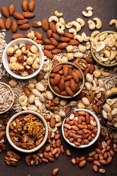 Selection of assorted raw nuts and various seeds in bowls on brown stone background from above, healthy source of energy, fat and vegetarian protein