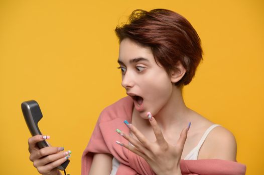 Angry pretty young brunette girl shouting into phone handset studio shot at yellow background
